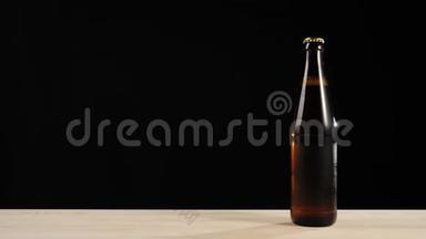 新鲜啤酒。 手把一个绿色的瓶子和美味的工艺啤酒放在棕色瓶子附近，啤酒放在木桌上